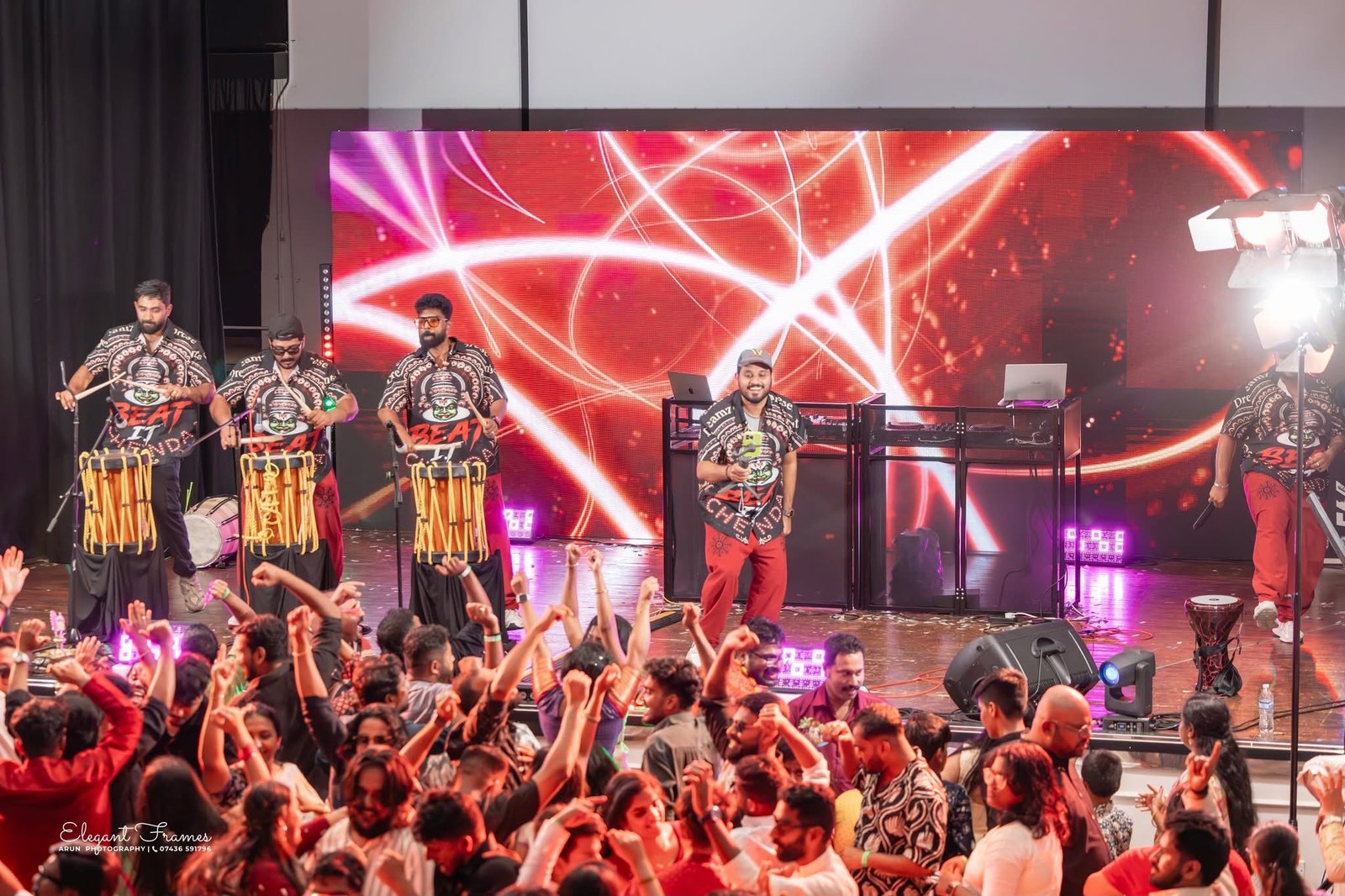 Chenda drummers performing on a red-lit stage as the crowd dances in front